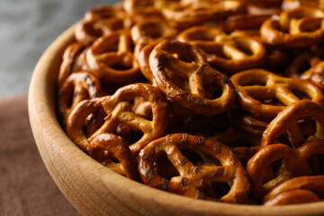 Wooden bowl with tasty cracker pretzels on napkin on black smokey background