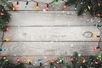 Christmas background - Christmas lights bulb and fir branch and snowflake on rustic wood table, frame border design. Merry Christmas and New Year holiday background. top view.