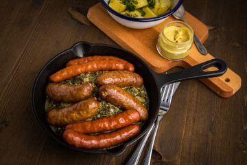 Oldenburger Grünkohl mit Pinkel, Kohlwurst, Senf und Kartoffeln in Gusseisen Pfanne auf Holz Tisch