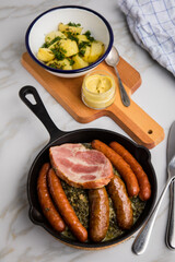 Oldenburger Grünkohl mit Pinkel, Kohlwurst, Kassler Schweine Nacken, Senf und Kartoffeln in Gusseisen Pfanne auf Marmor Tisch