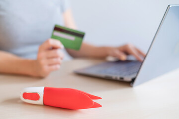 Fototapeta premium A faceless woman holds a credit card and a clitoral vibrator while sitting at a laptop. Online sex industry