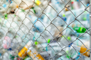 Blurred photo of pile of empty water plastic bottle in mesh fence recycle bin. Plastic bottle waste for recycle in recycling business. Plastic waste management. Reduce and reuse plastic. PET rubbish.
