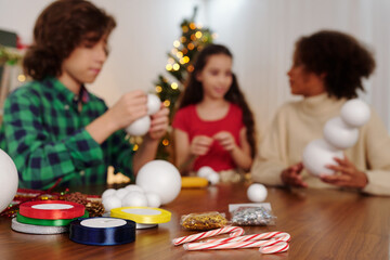 Colorful ribbons, candy canes and styrofoam balls on table in front of kids making Christmas decorations