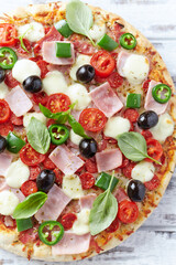 Pizza with ham, mozzarella cheese, cherry tomatoes, green and jalapeno pepper, black olives and fresh basil. Bright background. Top view. Close up.	