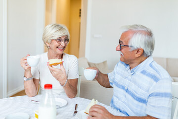 Fototapeta na wymiar Senior couple having breakfast and drinking coffee. Elderly couple having their meal at home. Mature woman holding piece of bread. An old man and woman sitting at the table, relaxing.