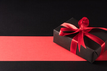 Black Friday sale shopping and Boxing Day concept, Gift box wrapped black paper and red bow ribbon present, studio shot isolated on red and dark background