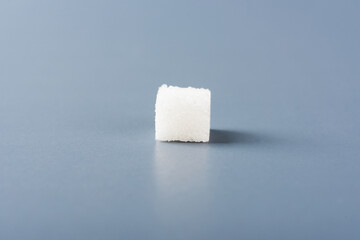 One white sugar cube sweet food ingredient, isolated on a gray background, health high blood risk of diabetes and calorie intake concept