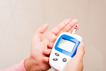 Closeup Hands woman measuring glucose test level check with blood on finger by glucometer at home she monitor and control high blood sugar diabetes and glycemic health care concept