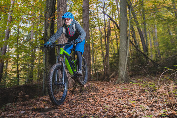 Fototapeta na wymiar Biker riding downhill with a modern electric bicycle or mountain bike in autumn or winter setting in a forest. Modern e-cyclist in woods.