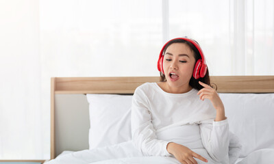 Young woman listening to music in red headphones on bed in the morning. Beautiful cheerful young woman listening to music in headphones. Girl listening songs at home on bed.