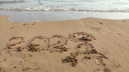 handwritten inscription 2020 and 2021 on sand of sea beach.