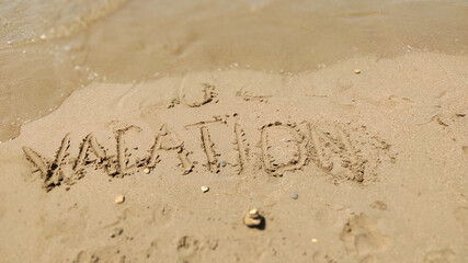 Text Vacation written in the sand of sea beach