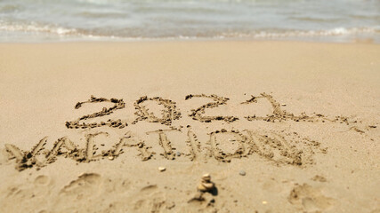 2021 Vacation handwritten inscription in sand of sea beach