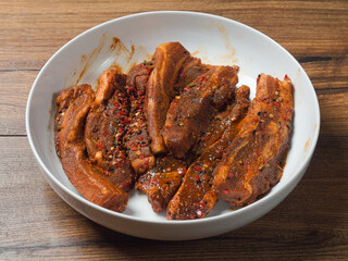 Raw pork belly slices in Korean style marinade on a white plate.