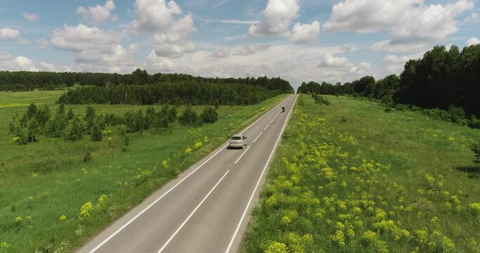 Two tourist on bike driving alone / travel on empty straight asphalt road freeway through dandelion field at summer sunny day. Aerial drone wide view.