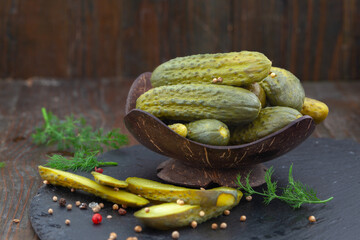 Pickled cucumbers with herbs and spices on wooden background. Homemade marinated cornichons in a bowl..