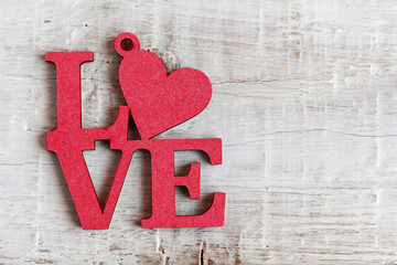 Red letters with a heart made of wood with the text Love on a white wooden background