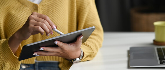 Closeup view of young woman holding digital tablet on hand and using electronic pen while working...