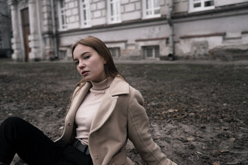 sad female student sitting on cold ground against the background of an educational institution,...