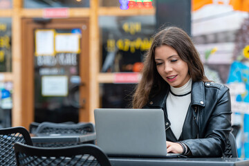 Fototapeta premium Portrait of a happy young woman relaxing in outdoor cafe and using a laptop