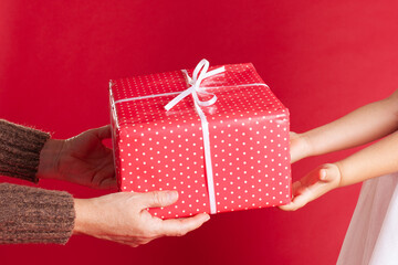 close up hands of a parent and child holding a Christmas gift, buying and packing gifts for Christmas on a red background.