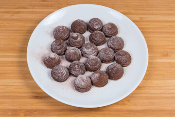 Chocolate truffles on white dish on the wooden surface