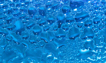 Transparent drops of pure water on a blue smooth surface.