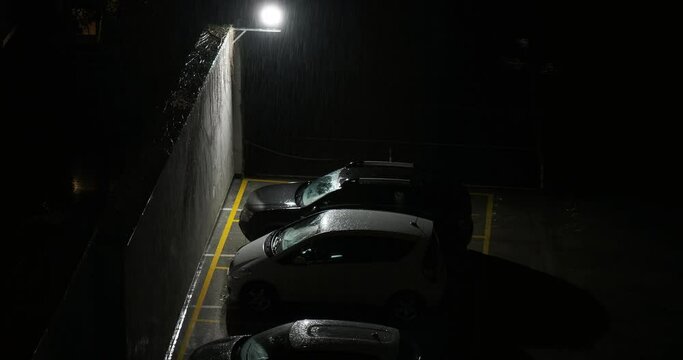 Rain falls on a September night on the city. Cars parked in an outdoor garage illuminated in the night by street lights.