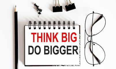 Think Big, Do Bigger Motivation notepad writing on white background with pencil and glasses