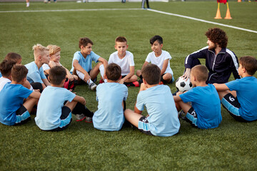 confident football trainer man teach, instruct kids boys in stadium. young caucasian boys...