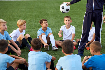 young team of sportive boys take a break during football competition, caucasian children talk, discuss, listen to trainer