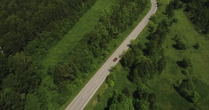 Two red sedan car driving alone / travel on empty asphalt road freeway through dense forest corridor at summer sunny day. Aerial drone wide view.