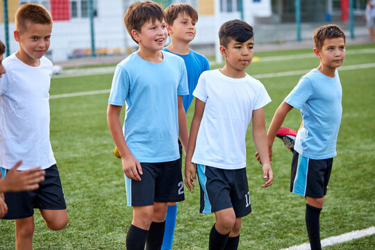 group of caucasian kid boys stretching legs before football game in stadium, they are in special sportive uniform, engaged in sport and healthy lifestyle from childhood