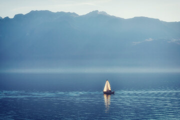 Sailing boat cutting through a tranquil misty mountain lake.
