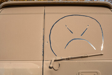 Ugly smile on dirty windscreen of car. Muddy vehicle, wash me concept.