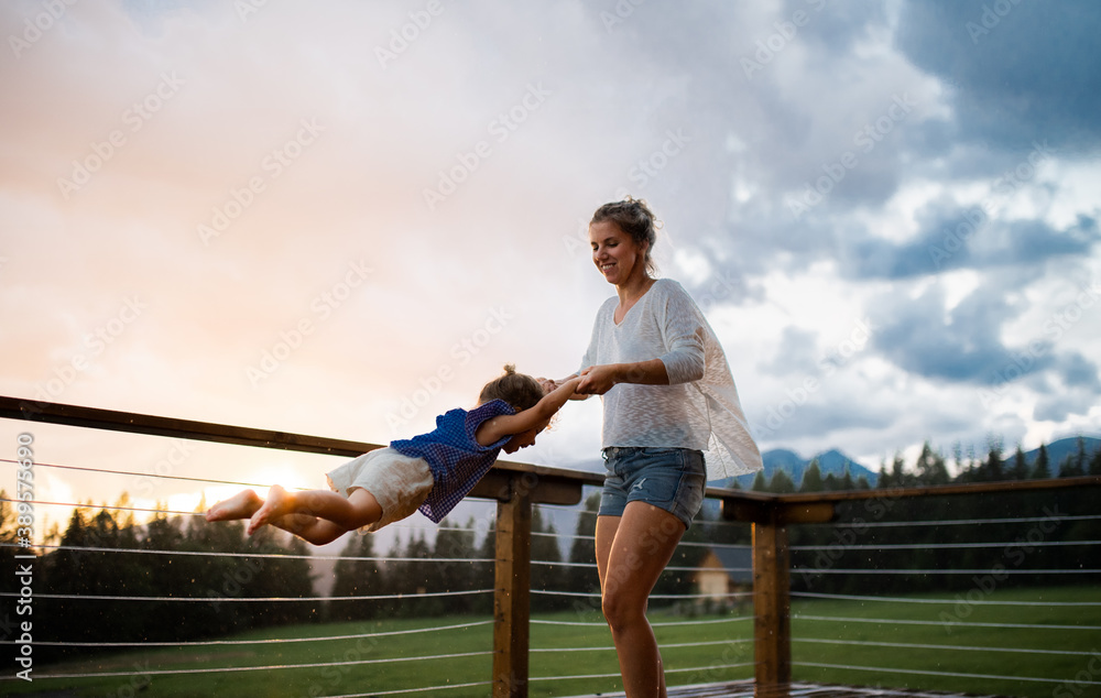 Wall mural Mother with small daughter playing on patio of wooden cabin, holiday in nature concept.