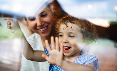 Small girl with mother by window, holiday in nature concept. Shot through glass.