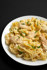 Homemade Chicken Fettuccine Alfredo on a white plate on a black background, side view. Copy space.