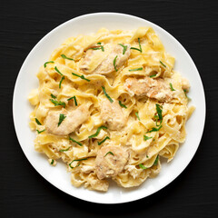 Homemade Chicken Fettuccine Alfredo on a white plate on a black surface, top view. Flat lay, overhead, from above.
