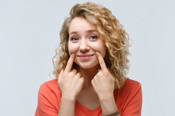 Young beautiful woman pretends to smile, stretches her mouth into a smile. Fake smile concept