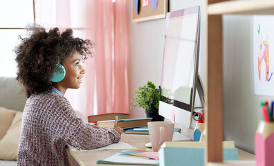 Fototapeta na wymiar African american kid girl online learning on computer at home. Cute mixed race child wearing headphones distance studying online class looking at pc screen. Virtual remote school for children concept.