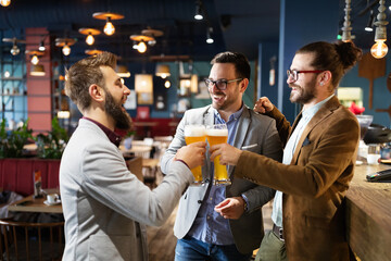 Leisure, friendship pub concept. Happy male friends drinking beer and clinking glasses at bar or pub