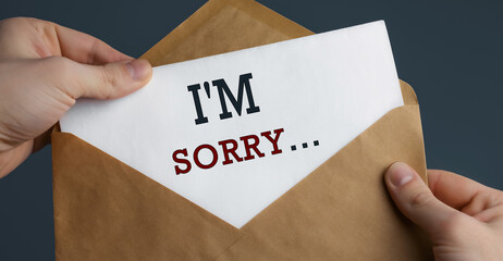 Male hands holding craft envelope with word SORRY on blue background
