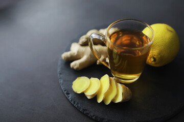 Ginger root whole and sliced. Ginger tea with lemon on the dark background. Fresh ginger root on stone background. Vitamins. Free space for your text.
