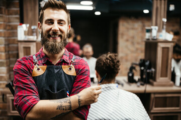 Portrait of happy young barber with client at barbershop and smiling.