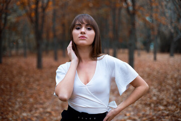 stylish young caucasian female with dark hair in the white blouse on the alley in autumn park, trees with orange leaves