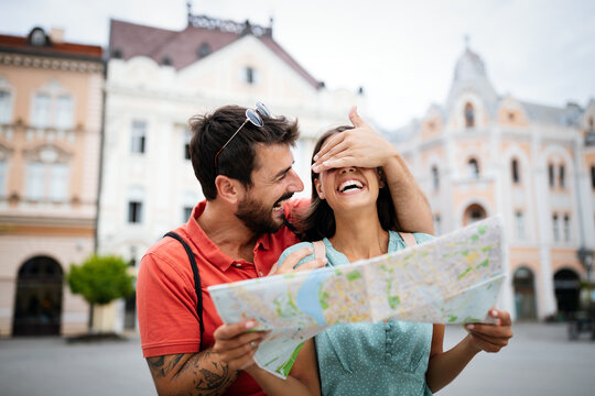 Happy young couple walking outdoors sightseeing and holding a map
