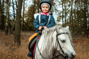 Little girl on a white pony on a background of nature. Jockey, hippodrome, horseback riding.