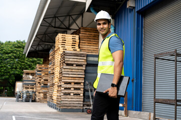 Portrait of young Indian worker working in logistic industry outdoor in front of factory warehouse....