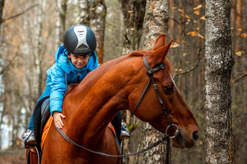 Little girl on an adult brown horse on the background of nature. Jockey, epodrome, horseback riding.